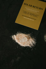 Load image into Gallery viewer, A gold instruction card labeled 'SOLAR RETURN' lies on a dark textured surface next to a small pile of pink salt with a white crystal.
