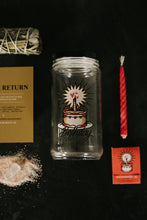 Load image into Gallery viewer, A clear glass jar with a printed birthday cake design sits on a black surface, surrounded by spell kit items, including a red spiral soy candle, a small red matchbook, a sage and sweetgrass bundle, salt with crystal, and a gold instruction card on a dark background.
